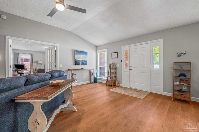 living room featuring light wood-style floors, ceiling fan, a textured ceiling, vaulted ceiling, and baseboards