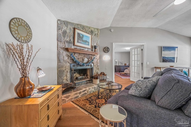 living room featuring a fireplace, vaulted ceiling, wood finished floors, and a textured ceiling