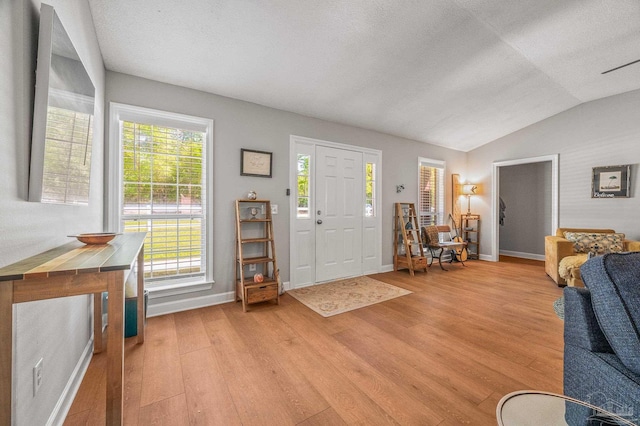 foyer entrance with light wood finished floors, baseboards, vaulted ceiling, and a textured ceiling