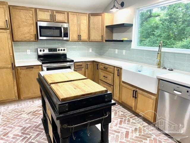 kitchen featuring decorative backsplash, brick floor, stainless steel appliances, light countertops, and open shelves