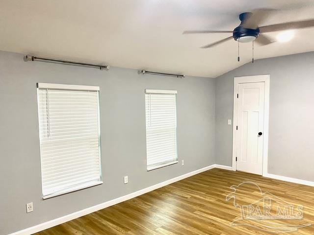 empty room featuring lofted ceiling, wood finished floors, a ceiling fan, and baseboards