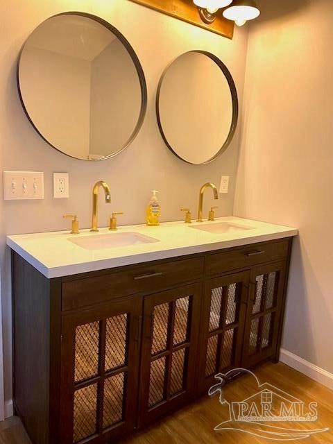 bathroom with double vanity, wood finished floors, a sink, and baseboards