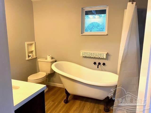 bathroom featuring toilet, wood finished floors, vanity, baseboards, and a soaking tub