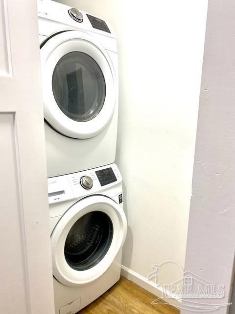 laundry area with light wood-type flooring, stacked washer / drying machine, and laundry area