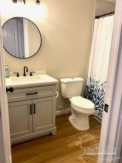 full bathroom featuring curtained shower, toilet, vanity, wood finished floors, and baseboards