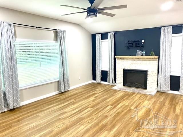 unfurnished living room featuring lofted ceiling, a fireplace, wood finished floors, a ceiling fan, and baseboards