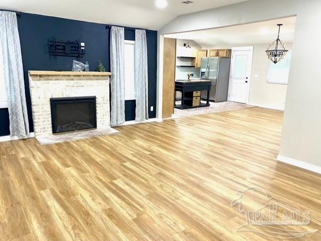 unfurnished living room featuring lofted ceiling, a fireplace, visible vents, baseboards, and light wood-type flooring