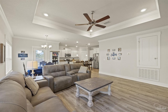 living room featuring light wood-type flooring, ceiling fan with notable chandelier, and a tray ceiling