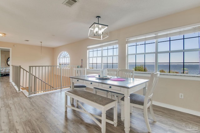 dining area with a notable chandelier, light hardwood / wood-style floors, a water view, and a textured ceiling