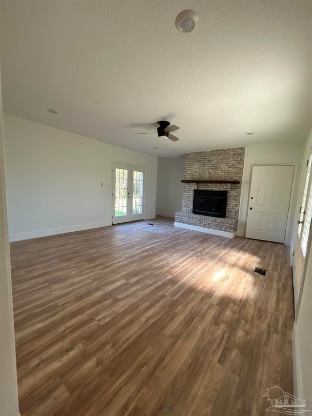 unfurnished living room featuring french doors, hardwood / wood-style flooring, a fireplace, and ceiling fan