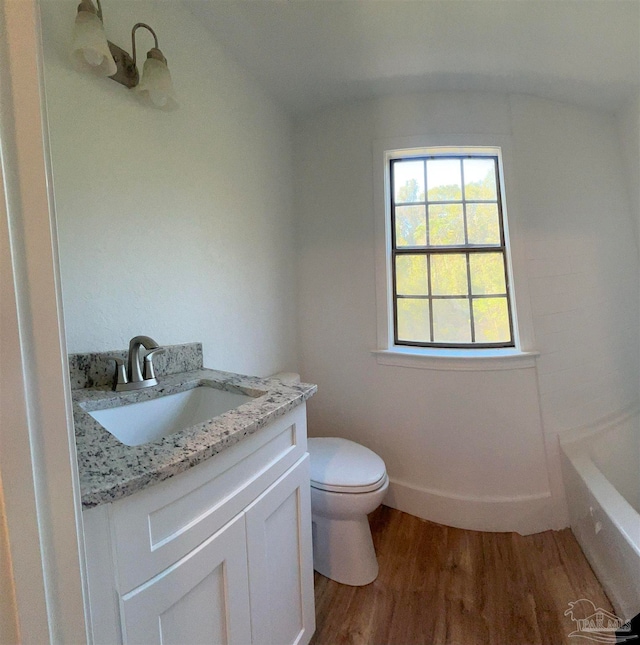 bathroom with a bathing tub, hardwood / wood-style floors, vaulted ceiling, toilet, and vanity