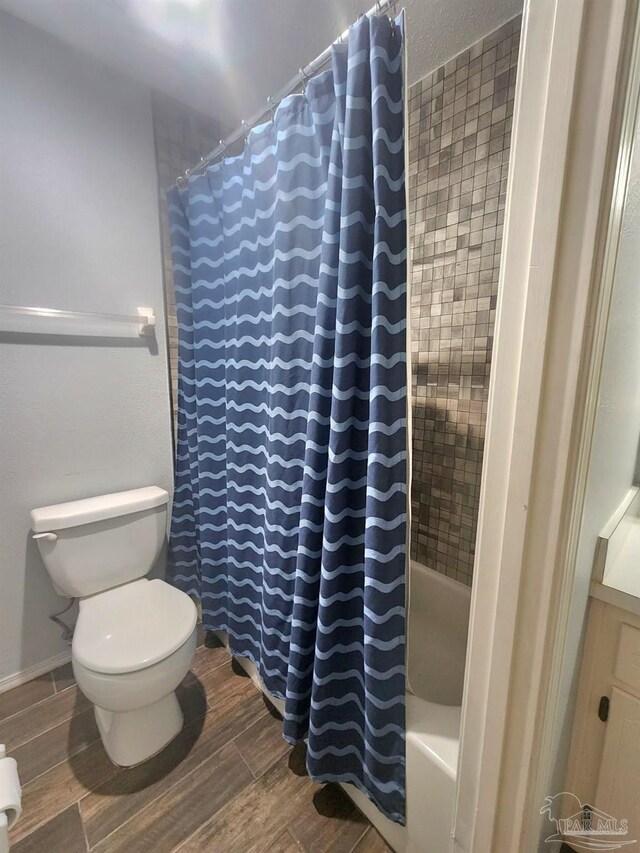 bathroom with shower / bath combo with shower curtain, toilet, and wood finished floors