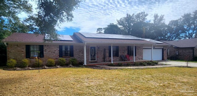 single story home with solar panels, covered porch, a garage, brick siding, and a front lawn