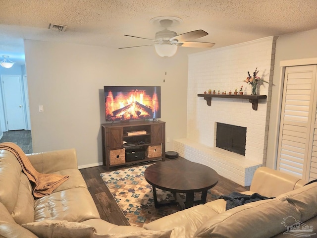 living area featuring a textured ceiling, a ceiling fan, visible vents, dark wood-style flooring, and a brick fireplace