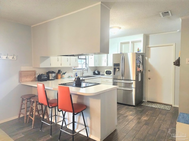 kitchen with visible vents, stainless steel refrigerator with ice dispenser, a sink, dark wood-style flooring, and a peninsula