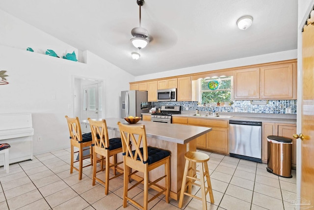 kitchen featuring light brown cabinets, a center island, backsplash, stainless steel appliances, and vaulted ceiling