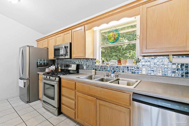 kitchen with light tile patterned floors, backsplash, stainless steel appliances, light brown cabinetry, and sink