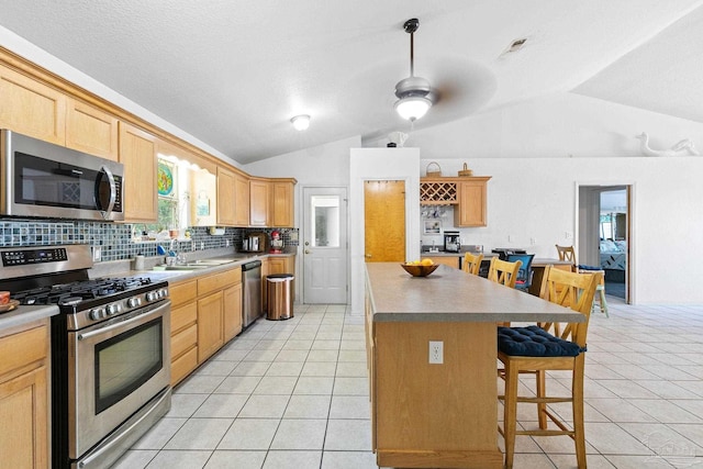 kitchen featuring stainless steel appliances, light tile patterned floors, a kitchen island, lofted ceiling, and ceiling fan