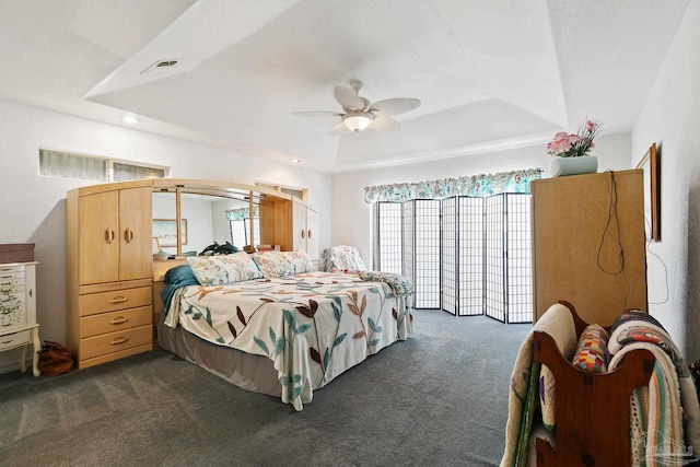 bedroom featuring ceiling fan, a raised ceiling, and dark carpet