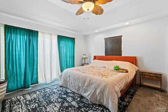 carpeted bedroom featuring multiple windows, ceiling fan, and a raised ceiling