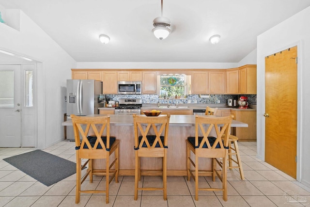 kitchen featuring light tile patterned floors, a center island, backsplash, ceiling fan, and appliances with stainless steel finishes