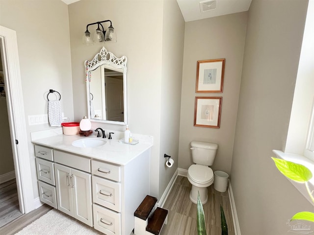 half bathroom with toilet, wood finished floors, vanity, baseboards, and visible vents