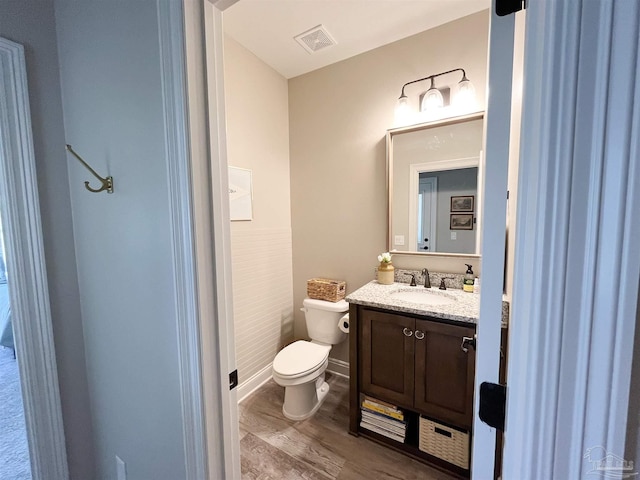 half bathroom featuring wood finished floors, vanity, baseboards, toilet, and visible vents