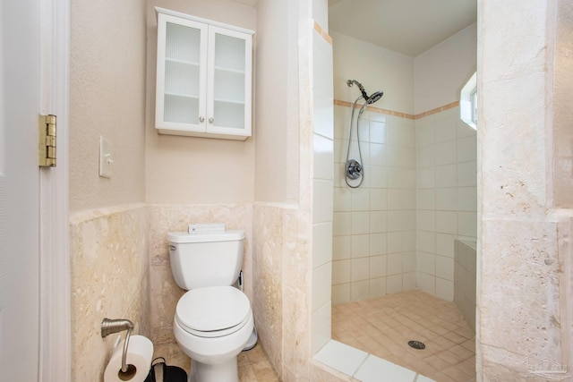 bathroom with tile walls, tiled shower, toilet, and tile patterned flooring