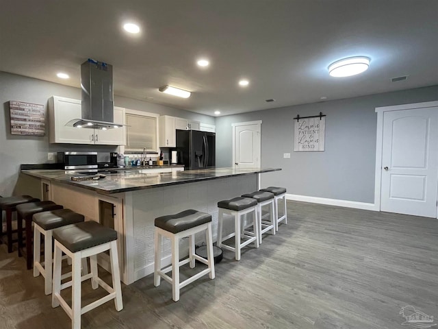 kitchen featuring island exhaust hood, white cabinetry, a breakfast bar, and black fridge with ice dispenser