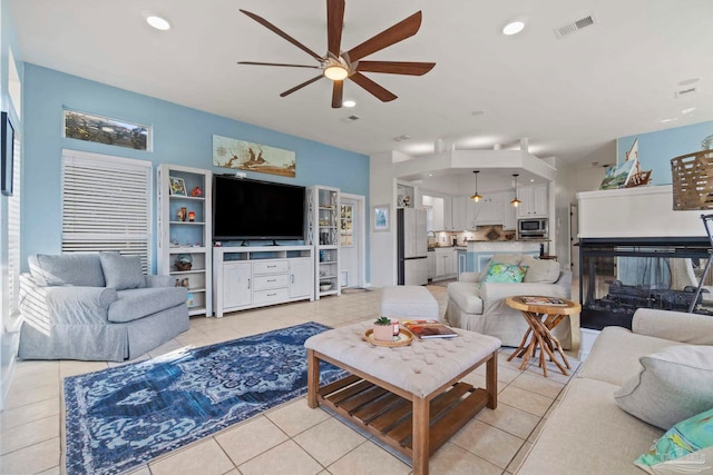 living room with a multi sided fireplace, light tile patterned floors, and ceiling fan