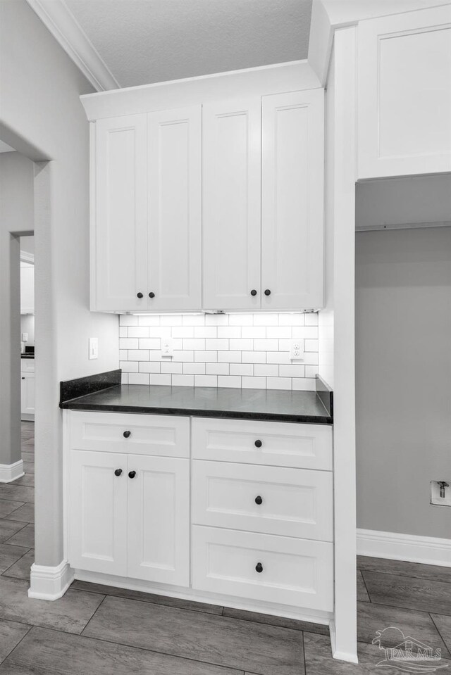 kitchen with white cabinetry, backsplash, dark wood-type flooring, and ornamental molding