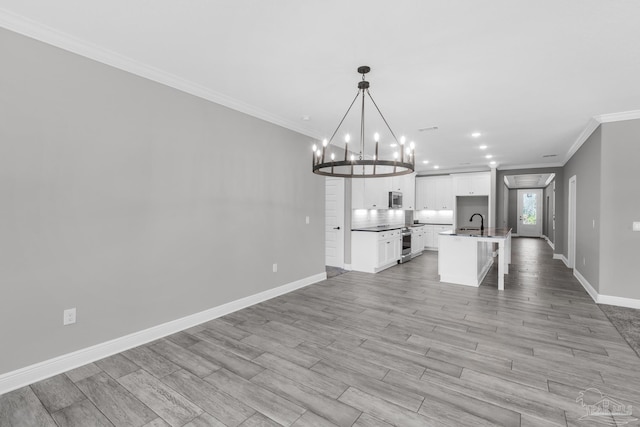 kitchen featuring white cabinetry, light wood-type flooring, decorative light fixtures, a center island with sink, and ornamental molding