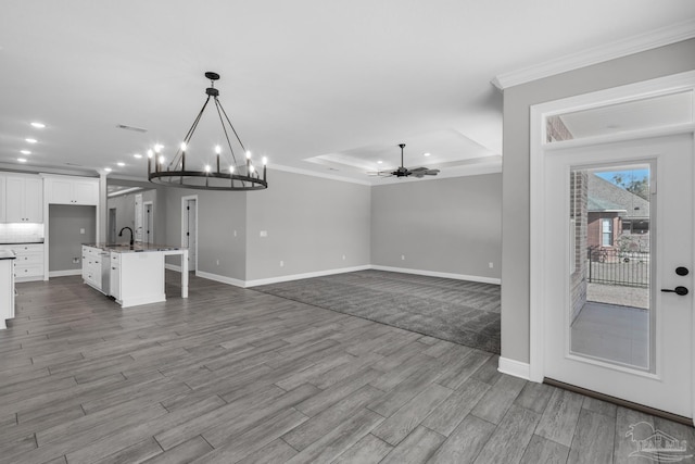 interior space with sink, a raised ceiling, light hardwood / wood-style flooring, crown molding, and ceiling fan with notable chandelier