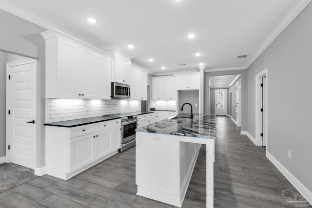 kitchen with ornamental molding, white cabinetry, stainless steel appliances, and an island with sink