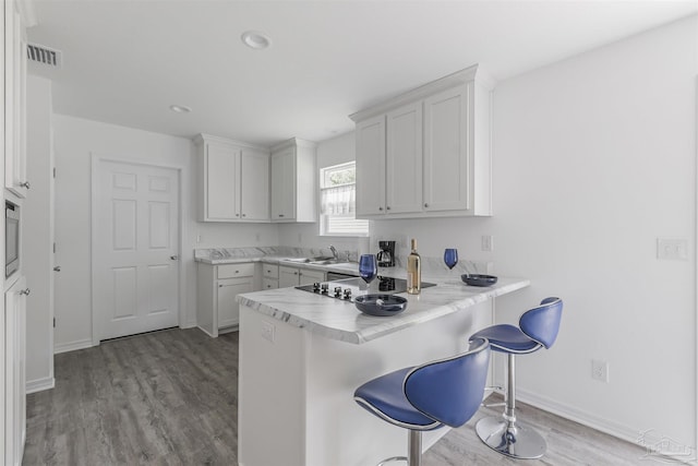 kitchen featuring visible vents, white cabinets, a kitchen breakfast bar, a peninsula, and light countertops