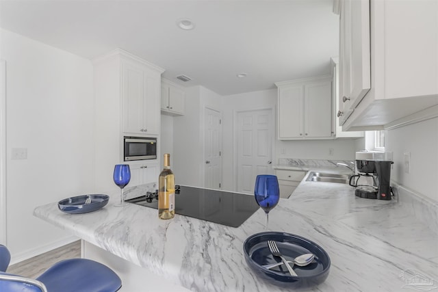 kitchen featuring light countertops, white cabinets, stainless steel microwave, and a sink