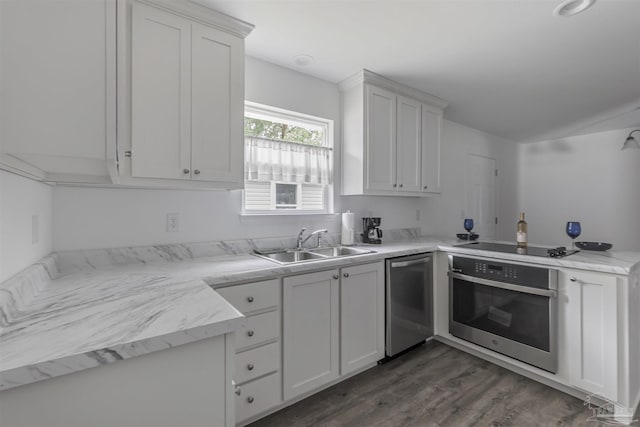 kitchen featuring a peninsula, dark wood-style flooring, a sink, white cabinets, and appliances with stainless steel finishes