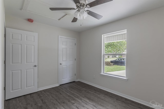 unfurnished bedroom featuring dark wood-style floors, attic access, a ceiling fan, and baseboards