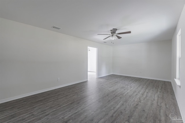 spare room with dark wood-style floors, ceiling fan, visible vents, and baseboards