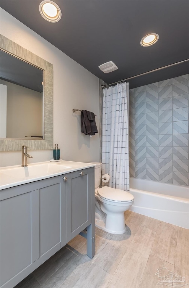 bathroom featuring visible vents, toilet, wood finished floors, shower / bath combination with curtain, and vanity