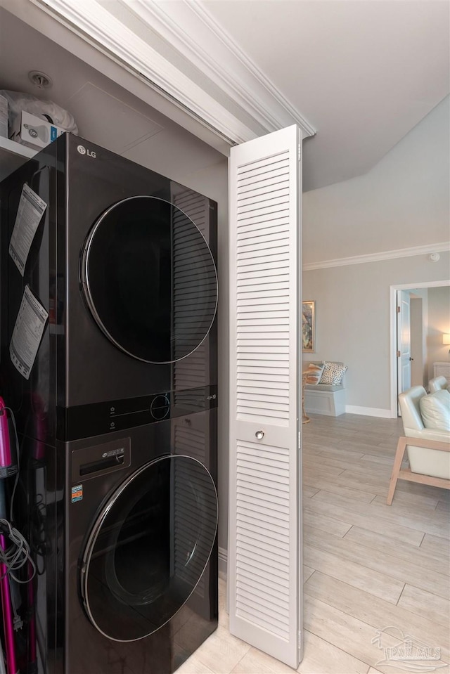 washroom featuring baseboards, laundry area, stacked washer / drying machine, crown molding, and light wood-type flooring