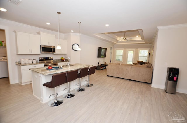 kitchen with ceiling fan, pendant lighting, an island with sink, stainless steel appliances, and white cabinets