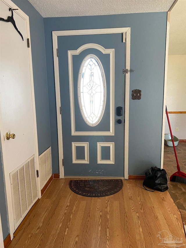 foyer entrance featuring a textured ceiling, wood finished floors, visible vents, and baseboards