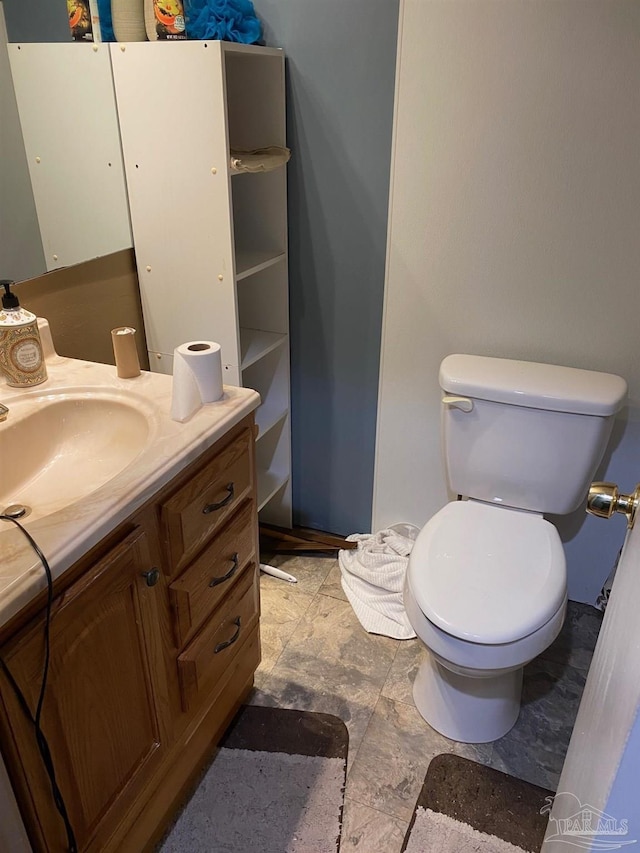 half bath with toilet, stone finish floor, and vanity