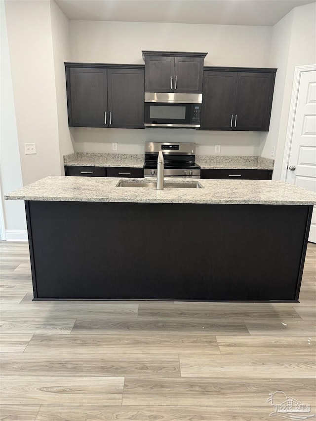 kitchen with light stone counters, sink, a center island with sink, and appliances with stainless steel finishes