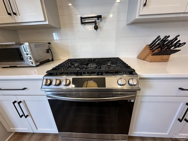 kitchen with tasteful backsplash, white cabinets, dark hardwood / wood-style floors, and stainless steel gas range