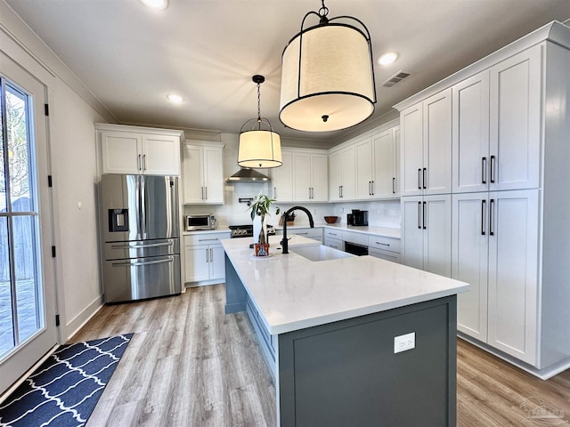 kitchen featuring white cabinets, decorative light fixtures, stainless steel appliances, an island with sink, and sink