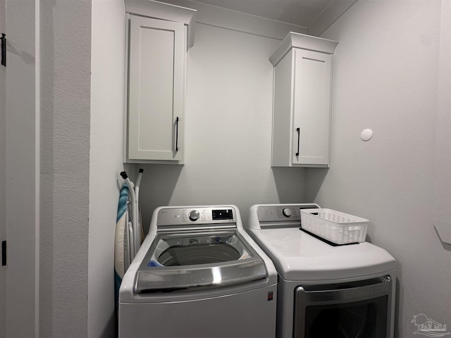 clothes washing area with washing machine and clothes dryer and cabinets