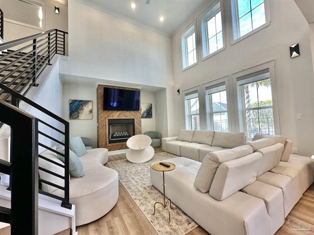 living room featuring light wood-type flooring, a large fireplace, crown molding, and a towering ceiling