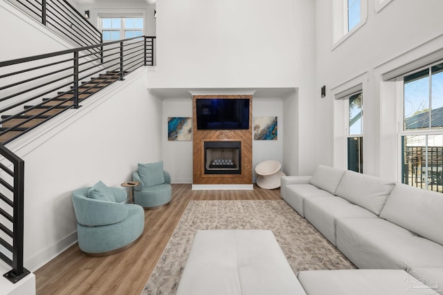 living room with light wood-type flooring, a wealth of natural light, a large fireplace, and a high ceiling